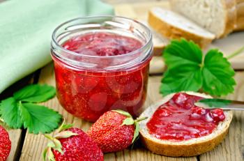 Strawberry jam in a glass jar, bread, strawberry with leaves, napkin, knife on background wooden plank