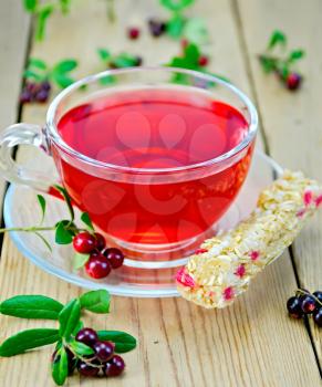 Tea in a glass cup with a bar muesli and berries lingonberries on a wooden boards background