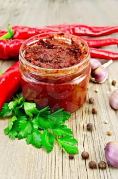 Tabasco in a glass jar, fresh red peppers, garlic, peppercorns, mustard seeds on the background of the old wooden boards