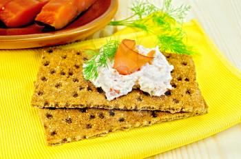 Two rye bread with mayonnaise and a slice of fish, dill, salmon pieces on a clay plate, the yellow cloth on the background of wooden boards