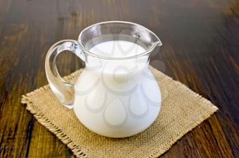 Milk in a glass jug on a napkin from burlap on background dark wooden board