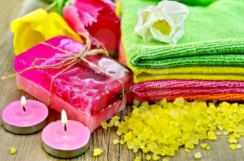 Two bars of homemade soap, towels, bath salts, two candles and tulips on a background of the old wooden boards