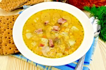 Pea soup in a plate, spoon, bread, napkin, smoked meat on the background of wooden boards