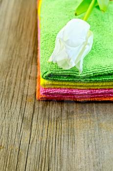 A stack of towels green, pink, orange and yellow with white tulip on an old wooden board