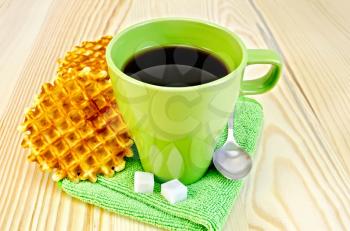 Two golden round waffles, green mug, sugar, spoon on green napkin on a background of wooden board