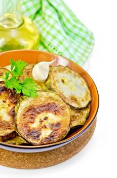 Fried zucchini in a ceramic bowl with garlic and parsley, oil in a bottle, napkin isolated on white background