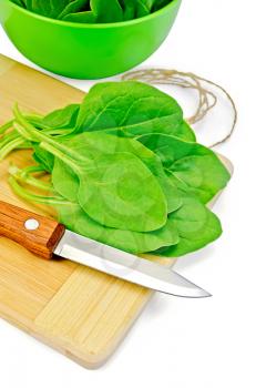 Green spinach on a small board with a knife, a bowl with spinach leaves, twine isolated on white background