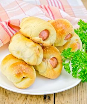 Sausage rolls on a plate with parsley, a napkin on a wooden boards background