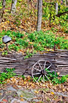 Cartwheels near the fence, the old cast iron pot on a background of trees, green grass and yellow autumn leaves