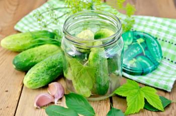 Cucumbers in a glass jar and on the table, garlic, tarragon, dill, cover with napkin, leaves cherries and currants on a wooden boards background