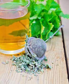 Herbal tea in glass mug, metal sieve with dry mint leaves, fresh mint leaves on the background of wooden boards