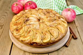 A sweet whole apple pie, napkin, cinnamon on a wooden boards background