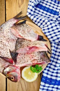 Bream whole peeled and sliced pieces on a round board, parsley, lemon, napkin on the background of wooden boards