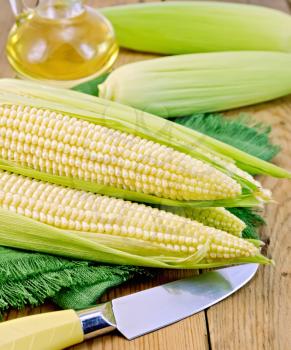 Corn on the cob on a green napkin, knife, oil in a carafe on the background of wooden boards