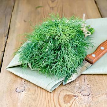 Fresh green dill on a napkin with a knife on the background of wooden boards