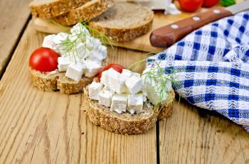 Slices of bread with feta cheese, tomato and dill, a napkin on a wooden boards background