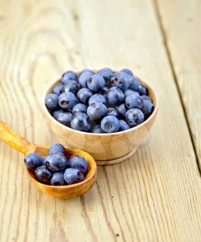 Blueberries in a wooden bowl and spoon on a wooden boards background