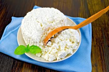 Cottage cheese in a bowl with basil and a wooden spoon on blue napkin on the background of wooden boards