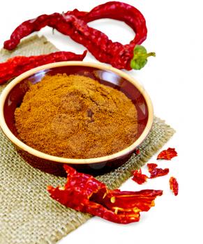 Red pepper powder in a clay bowl, red pepper pods on a napkin from a sacking isolated on white background