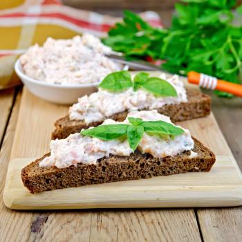 Sandwiches on two pieces of rye bread with cream of salmon and mayonnaise, basil, napkin, parsley on a wooden boards background