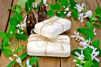 Two bottles of aromatic oil, two bars of white soap, twigs with leaves and white flowers of honeysuckle on a background of wooden boards