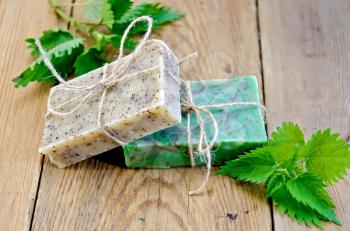 Two bars of homemade soap, tied with twine, nettle on the background of wooden boards