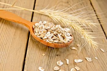 Rye flakes in wooden spoon, rye stalks on a wooden boards background