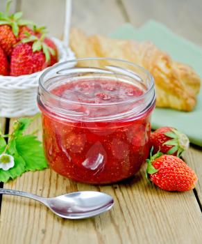 Strawberry jam in a glass jar, layered bun, strawberries in a basket, napkin, spoon on a wooden boards background