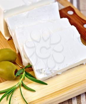 Feta cheese, knife, rosemary and olives on a wooden board on a background of brown checkered fabric