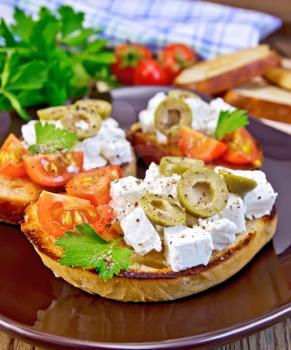 Slices of bread with feta, tomato and olives on a brown plate, napkin, parsley on a wooden boards background
