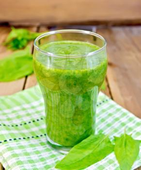 Glass cup with a cocktail of spinach, spinach leaves on a napkin on the background of wooden boards