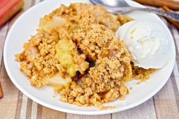 Rhubarb crumble and ice cream in a white plate, rhubarb stalks, cinnamon on linen tablecloth background
