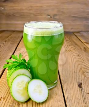 Cucumber juice in a tall glass, cucumbers, parsley on a wooden boards background
