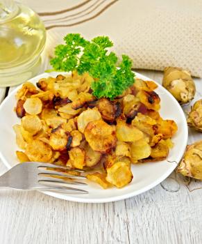 Jerusalem artichokes fried in a dish, fresh tubers, napkin, parsley, vegetable oil on a background of white wooden plank
