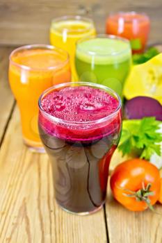Five tall glassfuls with juice of carrot, cucumber, beetroot, tomato and pumpkin, whole and sliced vegetables on background of wooden boards
