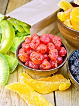 Candied cherries, melons, raisins in bowls, candied pomelo in a paper bag on a wooden boards background