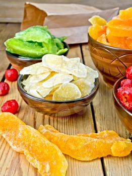 Candied ginger, pomelo, melon, cherries in bowls, paper bag on a wooden boards background