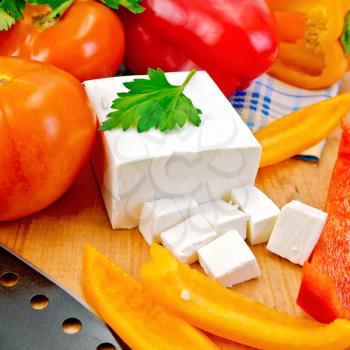 White brine cheese, black knife, parsley, tomatoes and red peppers on a wooden boards background
