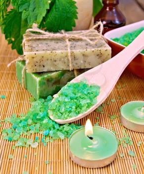 Bath salt in spoon, two bars of homemade soap with twine, oil bottle, nettle in a mortar, scented candle on a wooden boards background