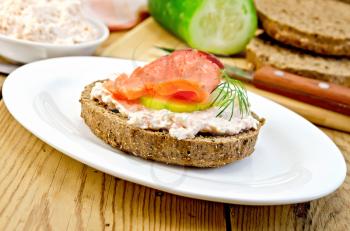 Sandwich from rye bread with cream, cucumber, dill and salmon on an oval plate on a wooden boards background