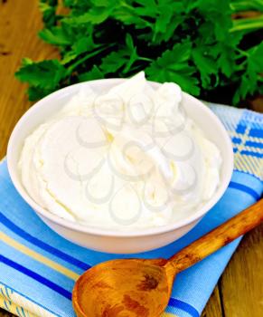 Thick yogurt in a white bowl, parsley, spoon, napkin on a wooden boards background