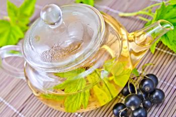 Tea in a glass teapot with leaves of black currant, berries and green leaves of black currant on a background bamboo napkin