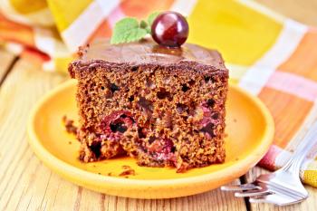 Chocolate cake with cherries and mint, fork, napkin on a wooden boards background