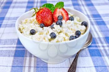 Cottage cheese in a white bowl with strawberries, blueberries and mint, a spoon against a background of blue linen tablecloth