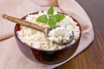 Cottage cheese in a wooden bowl with a spoon and mint on a cloth on a wooden boards background