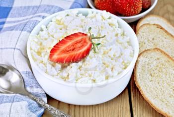 Cottage cheese in a white bowl with strawberries, a spoon, napkin, bread on a wooden boards background