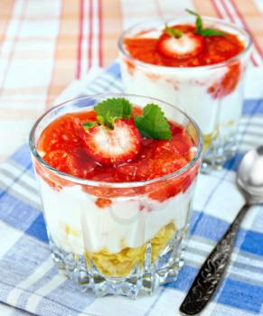 Dairy dessert with strawberries, corn flakes and yogurt in two glassful, spoon, blue napkin, strawberries in a bowl on blue linen tablecloth background