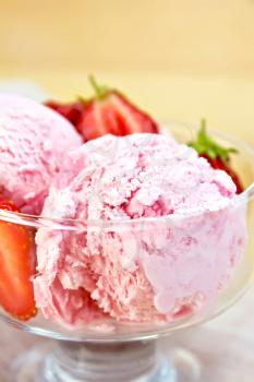 Strawberry ice cream in a glass bowl with strawberries on a napkin on a wooden boards background
