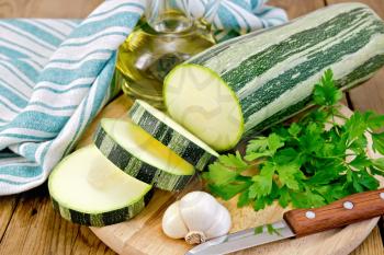 Green striped zucchini, garlic, a bottle of vegetable oil, parsley, green napkin, knife on a wooden boards background