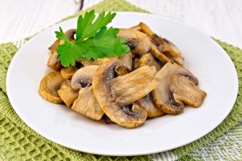 Champignons fried in a plate with a leaf of parsley on a napkin on the background light wooden boards